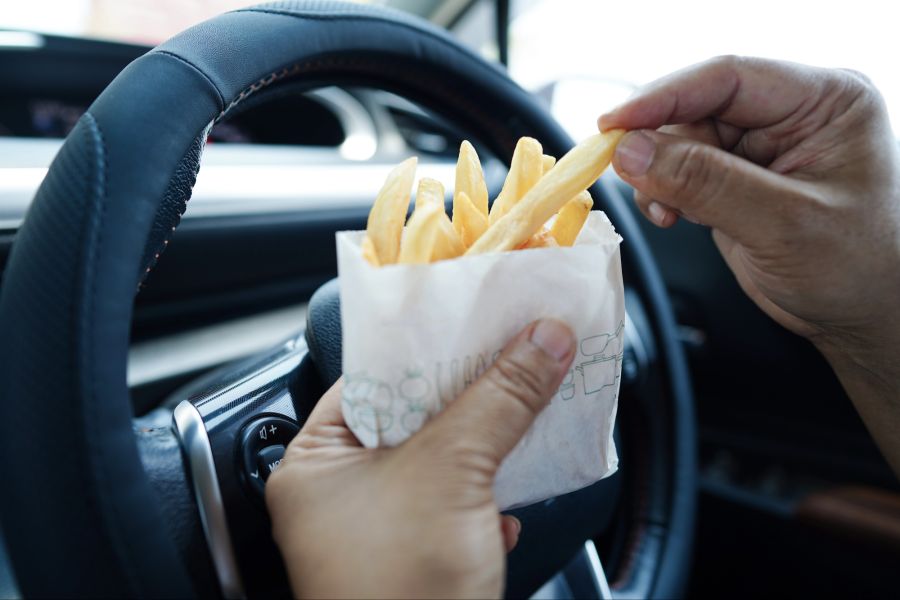 Person isst Pommes im Auto