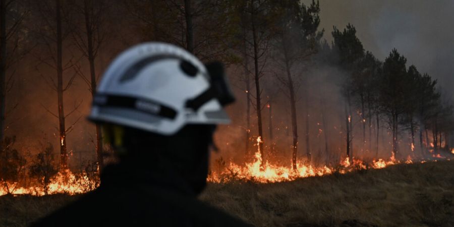 ARCHIV - Ein Feuerwehrmann geht vor brennenden Bäumen vorbei, während in der Nähe von Marcheprime, außerhalb von Bordeaux, Frankreich, ein Waldbrand wütet. Foto: Emma Da Silva/AP/d...
