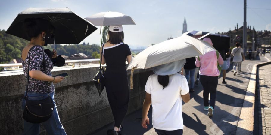 Touristen aus China schuetzen sich mit einem Schirm gegen die Sonne.