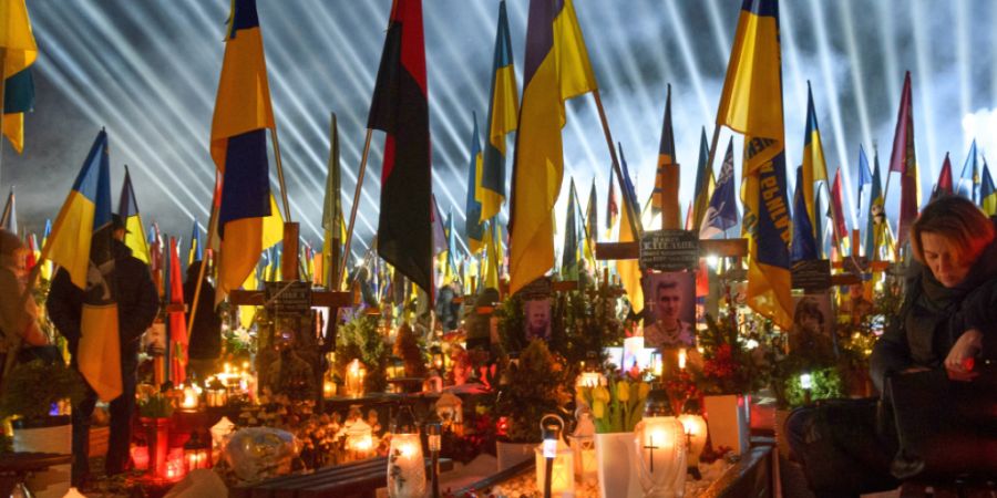 Flutlichter leuchten über den Gräbern der gefallenen Soldaten, während Menschen am Vorabend des vierten Jahrestages der russischen Invasion Kerzen anzünden. Foto: Mykola Tys/AP/dpa