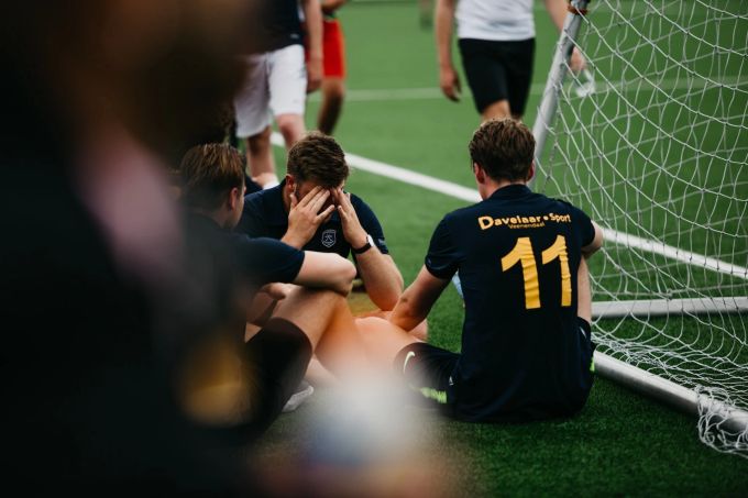 Zu Frustration und innerem Rückzug kann es in vielen Kontexten und Jobs kommen – nicht nur im Büro. Fussball Feld Team Männer sitzen Frust