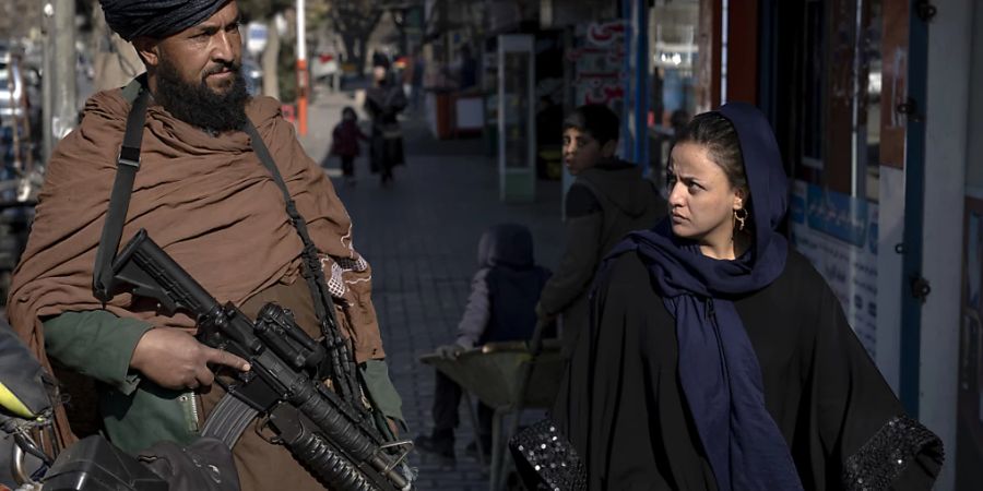 dpatopbilder - Ein Taliban-Kämpfer steht Wache, während eine Frau vorbeiläuft. Jüngste Entscheidungen der Taliban über afghanische Frauen, darunter das Verbot der Arbeit für Nichtregierungsorganisationen, lösten Proteste in den Grossstädten aus. Foto: Ebrahim Noroozi/AP/dpa