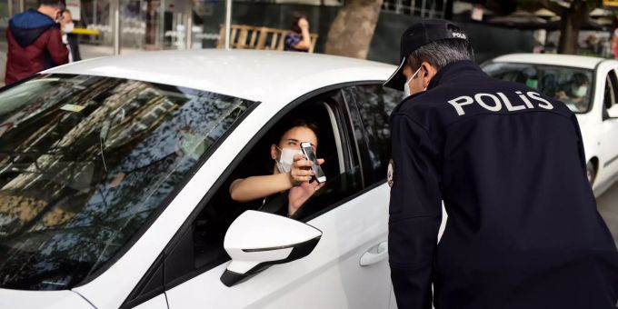 Ein Polizist schaut auf das Smartphone eines Autofahrers an einem Kontrollpunkt im Stadtzentrum. Coronavirus - Türkei