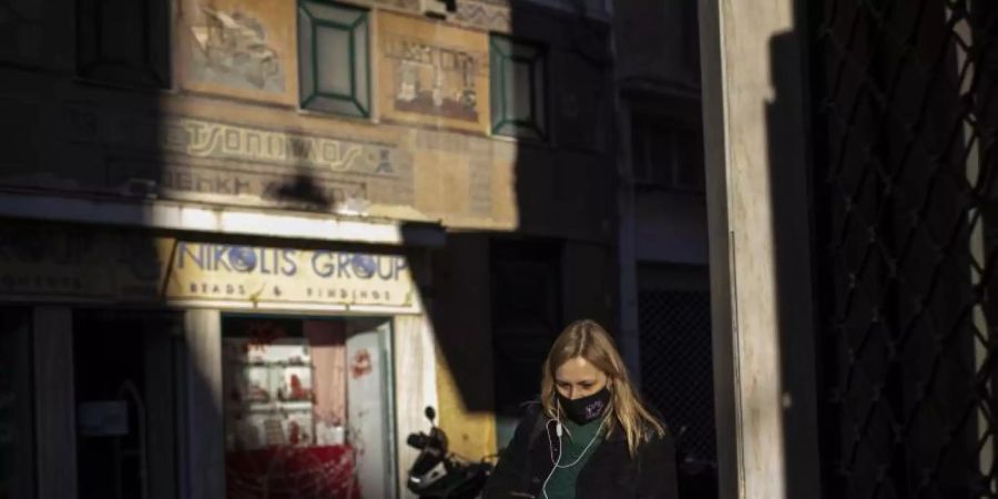 Eine Frau, die eine schützende Gesichtsmaske trägt, geht im Zentrum von Athen. Foto: Petros Giannakouris/AP/dpa