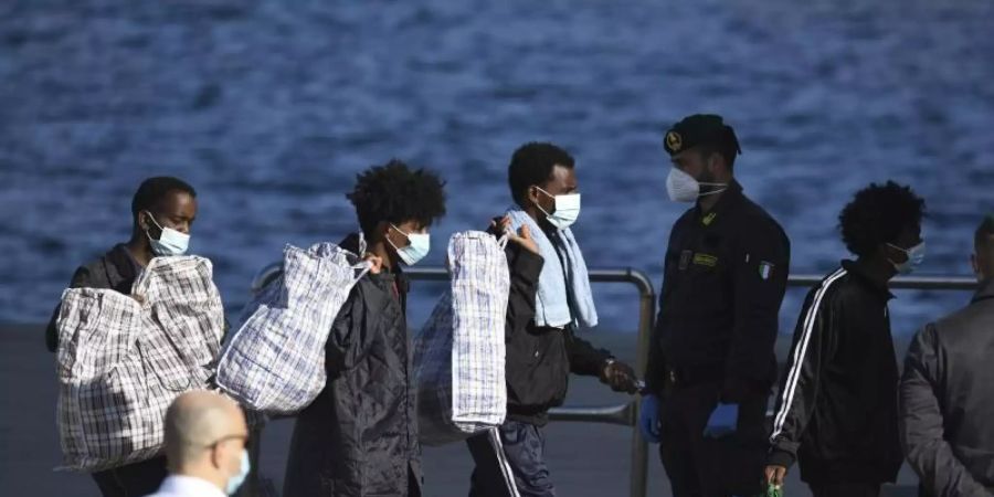 Migranten tragen ihre Habseligkeiten von Bord des Schiffes GNV Azzurra auf der sizilianischen Insel Lampedusa. Foto: Salvatore Cavalli/AP/dpa/Archivbild