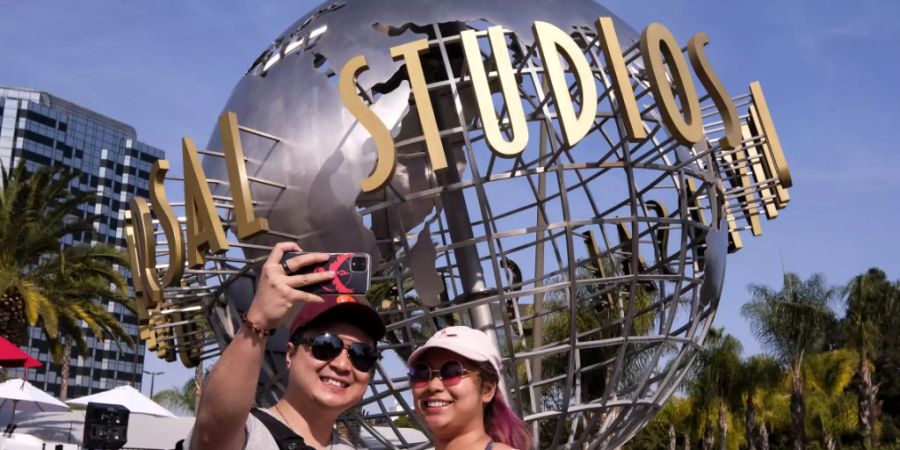 Ein Paar fotografiert sich vor dem Schriftzug Universal Studios Hollywood auf einer Weltkugel-Skulptur. Am Dienstag hob Kalifornien die meisten seiner COVID-19-Beschränkungen auf und läutete das ein, was als die «Grosse Wiedereröffnung» des Staates bezeichnet wurde. Foto: Ringo H.W. Chiu/FR170512 AP/dpa