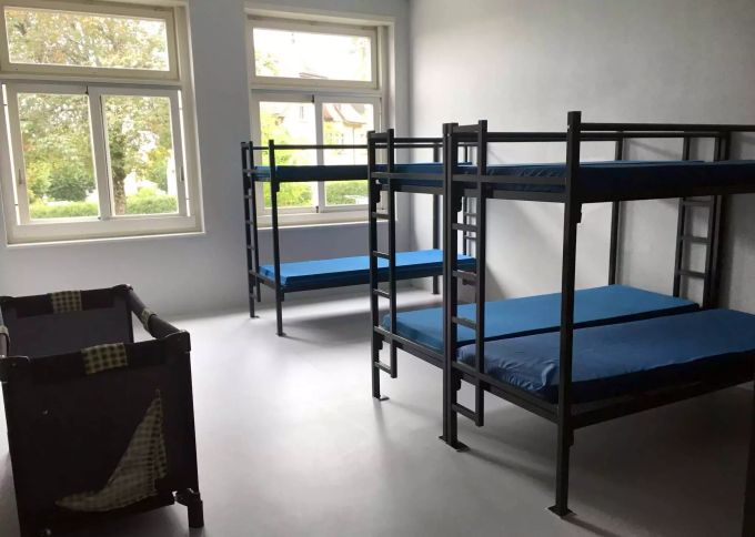 Stockbetten und ein Reisebett für Kleinkinder stehen in einem leeren Raum im Aslyzentrum Boudry NE in einem Workshop Nähen. Asyl in der Schweiz