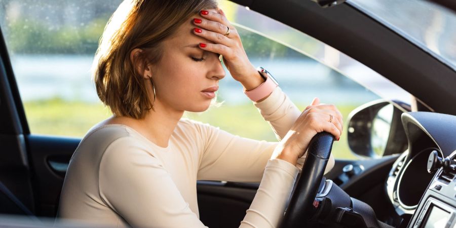 Frau mit Kopfschmerzen am Lenkrad im Auto