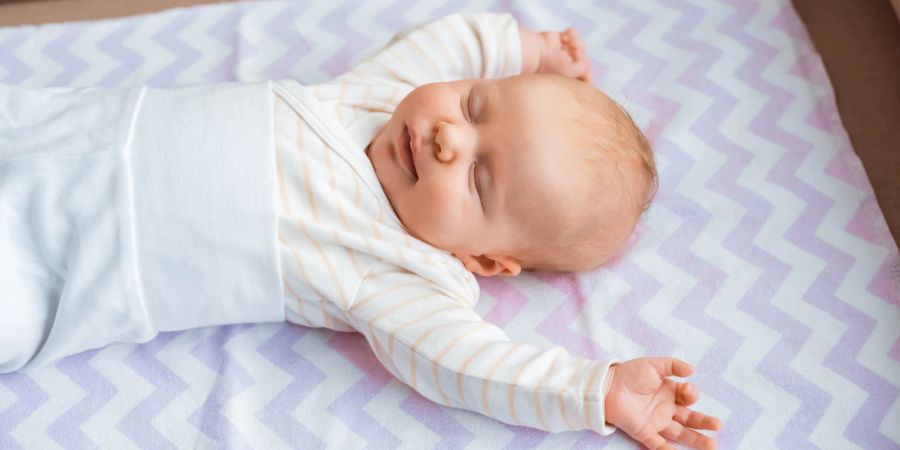 Ein Baby schläft lächelnd mit ausgestreckten Armen.