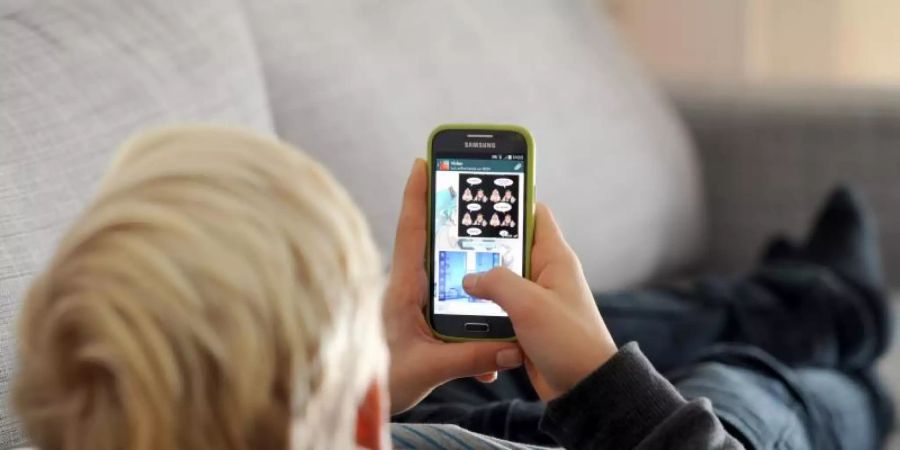 Ein Jugendlicher liegt auf einem Sofa und schaut auf sein Smartphone. Foto: Tobias Hase/dpa