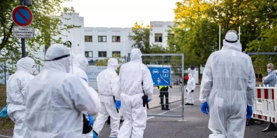 Beamte der Polizei und des Ordnungsamtes betreten in Schutzanzügen die Flüchtlingsunterkunft in St. Augustin. Foto: Marcel Kusch/dpa
