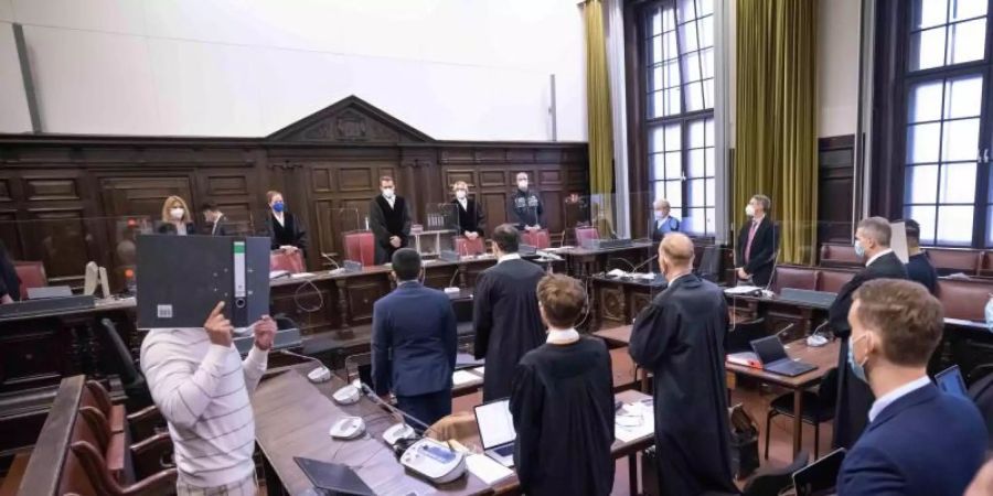 Der Hauptangeklagte (l, in Untersuchungshaft), sowie weitere Angeklagte, Anwälte und Prozessbeteiligte, stehen vor Beginn des Prozesses im Gerichtssaal. Foto: Christian Charisius/dpa