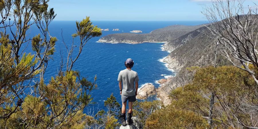 Mann auf Klippe vor fernem Strand