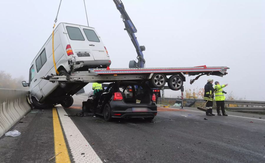 Demolierte Fahrzeuge stehen an einer Unfallstelle auf der Autobahn A7 auf einer Brücke im Nebel.