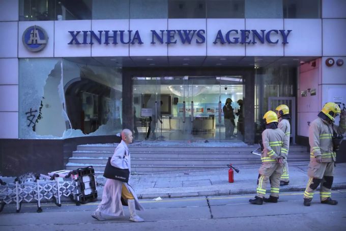 Feuerwehrleute stehen vor den Büros der chinesischen Nachrichtenagentur Xinhua, nachdem deren Fenster von Demonstranten beschädigt wurden. hongkong