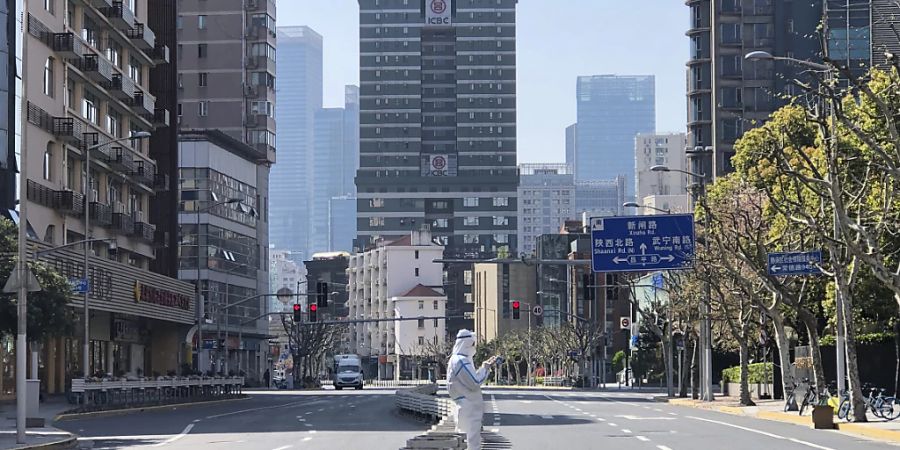 dpatopbilder - Ein Mann in einem Schutzanzug steht auf einer fast menschenleeren Strasse in einem abgesperrten Gebiet im Westen von Shanghai. Foto: Chen Si/AP/dpa