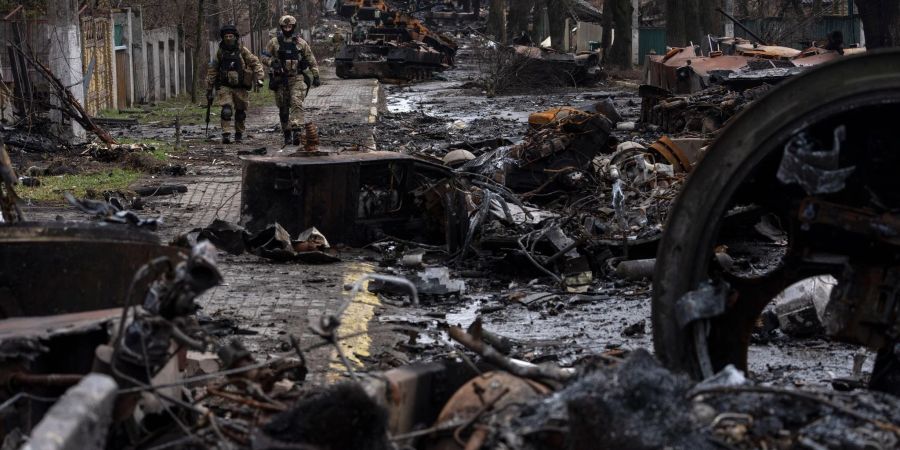 Zwei ukrainische Soldaten inspizieren in Butscha eine mit zerstörten russischen Militärfahrzeugen übersäte Strasse.