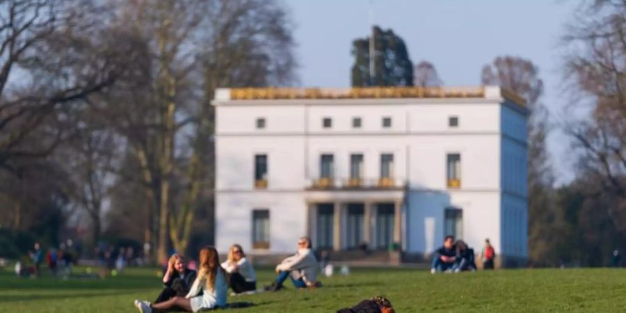 Menschen geniessen das sonnige Wetter auf einer Wiese vor dem Jenisch-Haus in Hamburg. Foto: Jonas Walzberg/dpa
