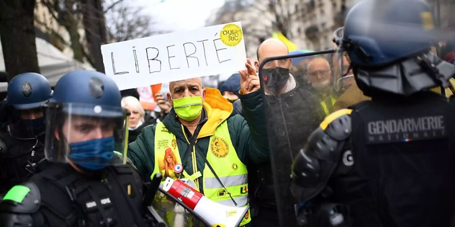 Ein Demonstrant in Paris hält vor Polizisten ein Schild mit der Aufschrift «Freiheit» in die Höhe. Foto: Christophe Archambault/AFP/dpa