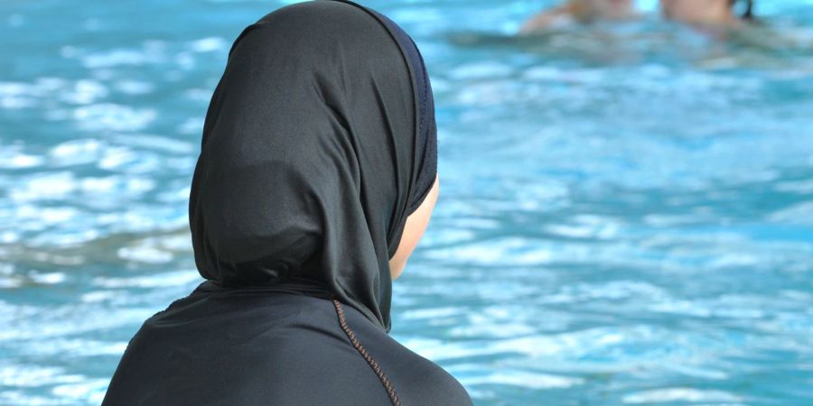 Eine muslimische Schülerin sitzt in einem Ganzkörperbadeanzug (Burkini) am Rande eines Schwimmbeckens. In Frankreich ist erneut ein Streit um Burkinis ausgebrochen.