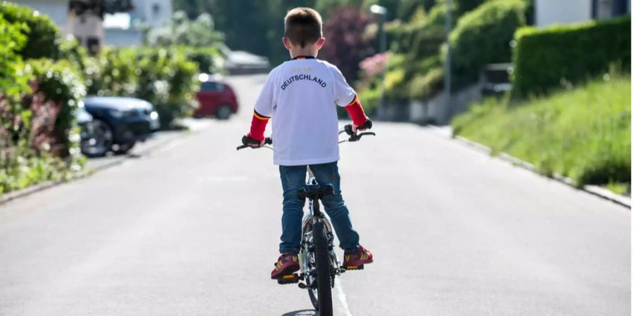 Ein junge mit einem deutschen Fussballtrikot fährt mit dem Fahrrad durch die Nachbarschaft.