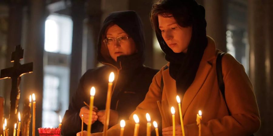 Zwei Frauen zünden Kerzen zum Gedenken an die Opfer des Angriffs auf eine Berufsschule auf der Halbinsel Krim in einer Kirche an.