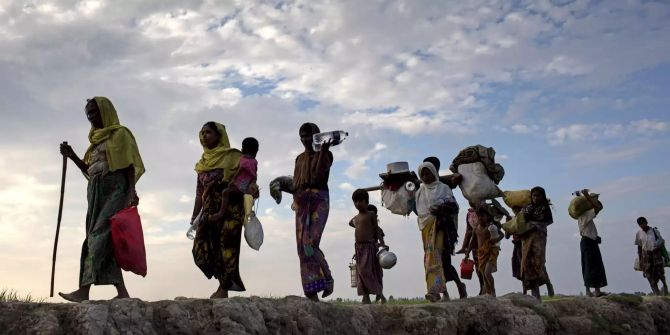 Rohingya-Flüchtlinge gehen mit ihrem Gepäck über ein Reisfeld.