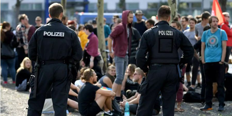 Zwei Polizisten stehen am Landtag in Chemnitz (D) vor einer Gruppe junger Leute.