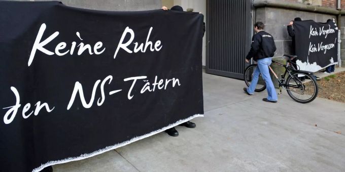 Aktivisten protestieren vor einem Aachner Gericht gegen Verbrecher des Nazi-Regimes.