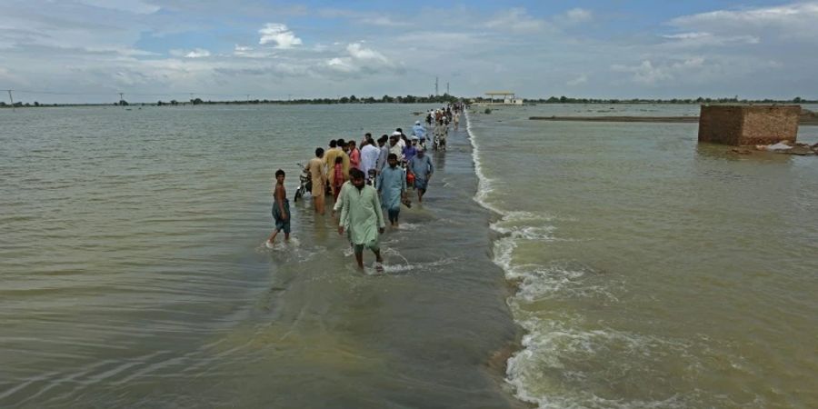 People walk along a flooded road to escape their villages in Punjab province