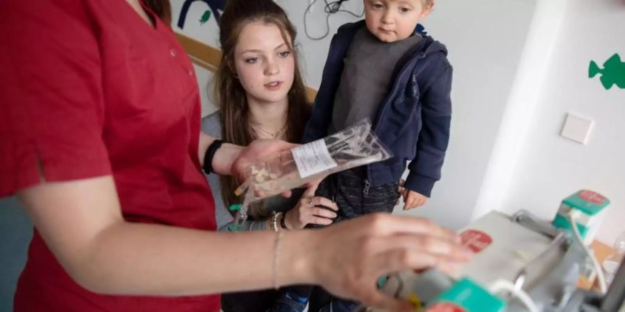 Levin Gebhardt sitzt auf Schoss seiner Mutter Lea, während eine Pflegerin eine Infusion vorbereitet. Im Alter von drei Monaten erkrankte der heute Dreijährige an Leukämie. Foto: Marijan Murat