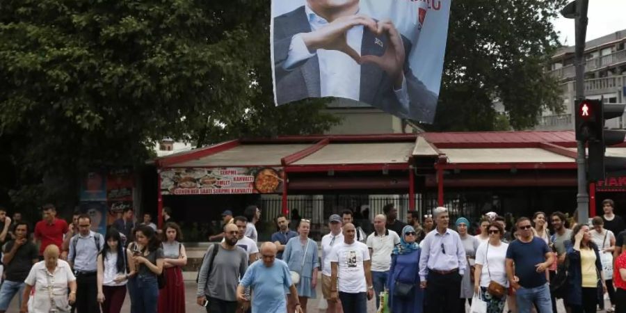 Menschen gehen unter einem Wahlplakat des Bürgermeisterkandidaten Imamoglu der Mitte-Links-Partei CHP entlang. Imamoglu hatte die Bürgermeisterwahl in Istanbul am 31. März 2019 knapp vor seinem Herausforderer Yildirim gewonnen. Allerdings annullierte die Hohe Wahlkommission die Abstimmung und ordnete eine Wiederholung am 23. Juni 2019 an. Foto: Lefteris Pitarakis/AP