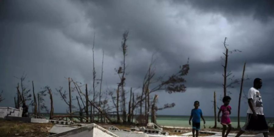 Menschen gehen an den Trümmern auf einem Friedhof auf den Bahamas vorüber. Foto: Ramon Espinosa/AP
