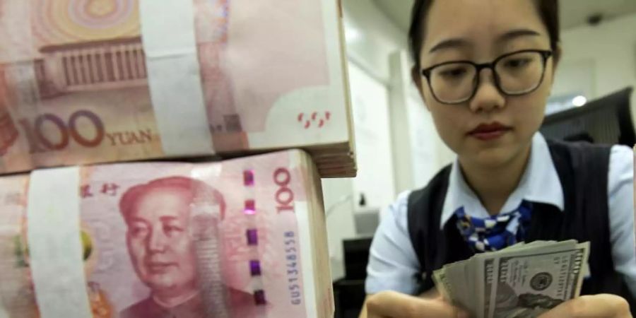 Eine Bankmitarbeiterin in Hai'an zählt US-Dollar-Banknoten neben einem Stapel von chinesischen 100 Yuan-Banknoten. Seit mittlerweile elf Handelstagen ist Chinas Währung auf Talfahrt. Foto: CHINATOPIX/AP