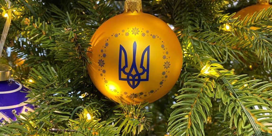 An einem geschmückten Baum hängt eine Kugel in den ukrainischen Nationalfarben und dem Dreizack als Wappen.