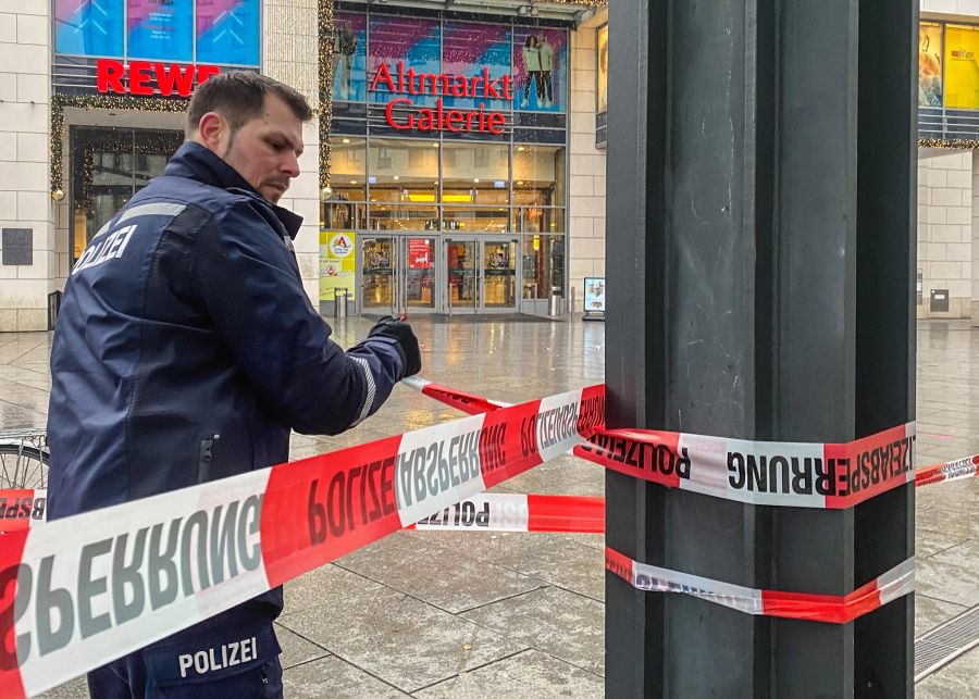 Ein Polizist sperrt die Altmarkt-Galerie während des Polizeieinsatzes mit Absperrband ab.