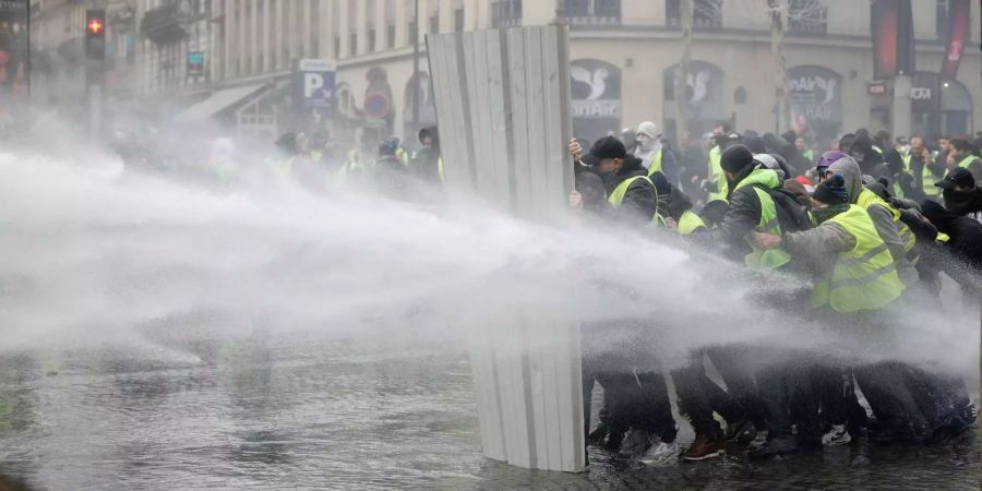 Demonstranten schützen sich mit einer Blechwand vor dem Wasserwerfer der Polizei.