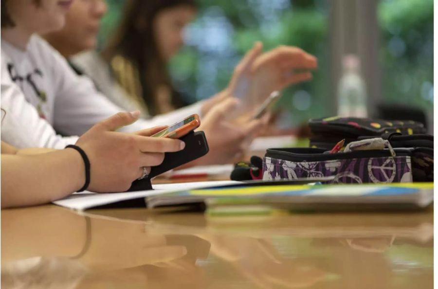 Schüler sitzen mit Handy an ihrem Platz in der Schule - Keystone