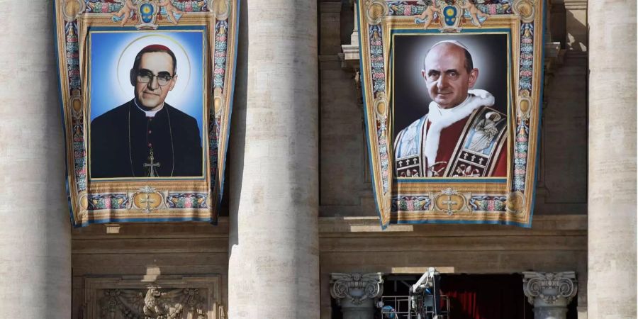 Die Wandteppiche des römisch-katholischen Erzbischofs Oscar Romero und Papst Paul VI. hängen von einem Balkon an der Fassade der Peterskirche im Vatikan.