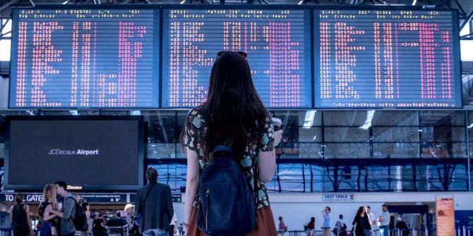 Ein Frau steht an einem Flughafen und schaut auf die Abflugstafel.