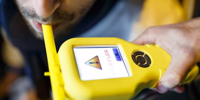 Ein Mann pustet in ein Atem-Alkoholtestgerät. alkohol test