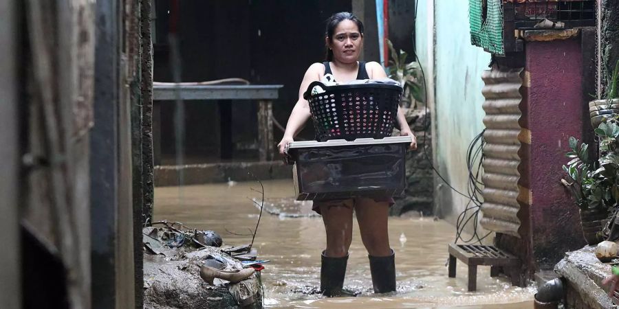 Eine Frau watet mit zwei Körben durch eine überflutete Strasse in der philippinischen Provinz Rizal.