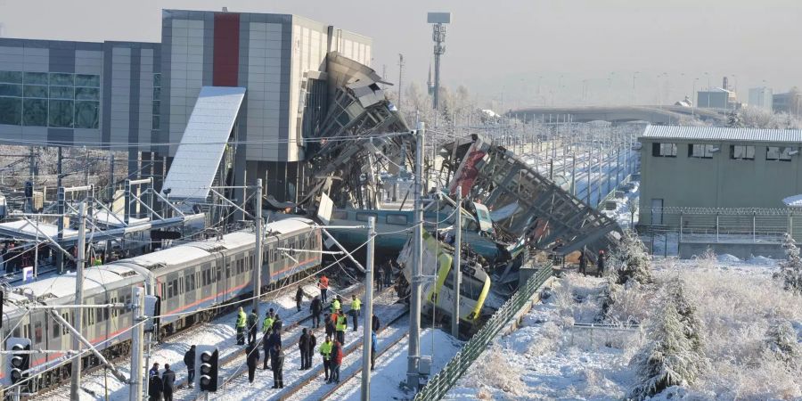 Mehrere beschädigte und entgleiste Wagons und eine Lokomotive liegen unter den trümmern eines Bahnhofs in Ankara im Gleisbett.