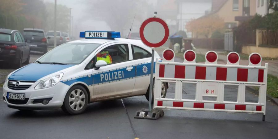 Ein Einsatzfahrzeug der Polizei steht neben einer Strassensperre.