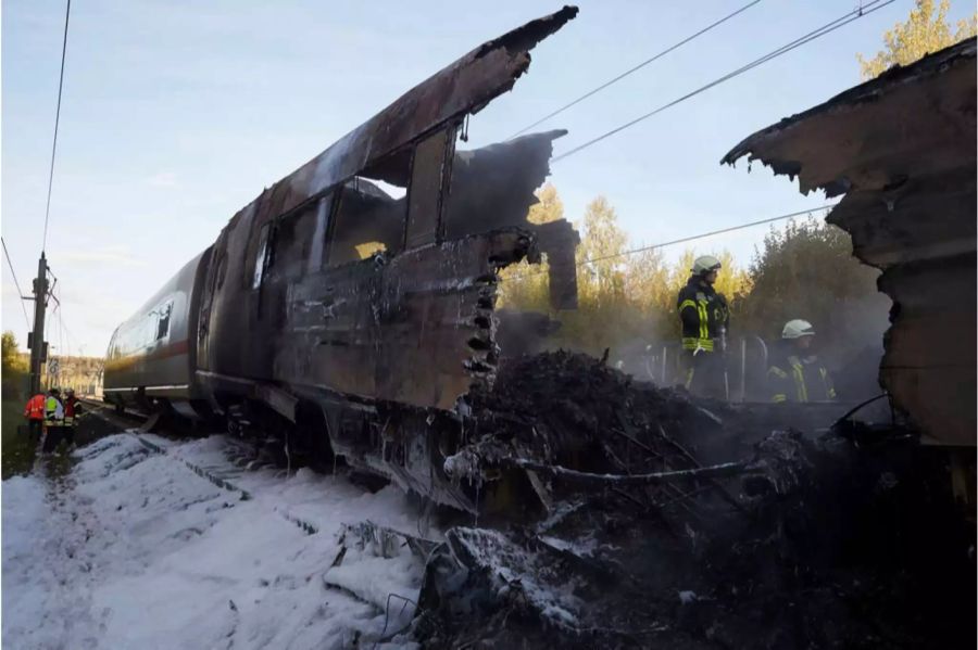 Zwei Feuerwehrmänner stehen in den Trümmern des abgebrannten ICE-Wagens.