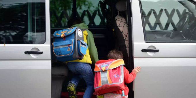 Zwei Kinder mit Schulranzen steigen in ein graues Auto. Zwei Kinder mit Schulranzen steigen in ein graues Auto.