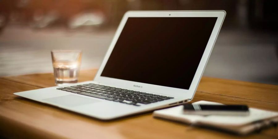 Ein Glas, Laptop und ein Notizbuch liegen auf einem Tisch.