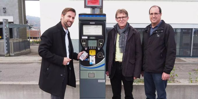 Adrian Plattner, CSO TWINT AG, zeigt gemeinsam mit Werner Spiri, Leiter Amts für Sicherheit, und Markus Rahm, Verkauf und Projekte Digitalparking AG, wie einfach es ist, mit der TWINT App seine Parkgebühren zu bezahlen. Menschen vor Parkautomat