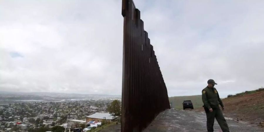 Der US-Grenzschutzbeamte Vincent Pirro geht am Ende der Grenzmauer entlang, die Tijuana in Mexiko (l) von San Diego in den USA trennt. Foto: Gregory Bull/AP