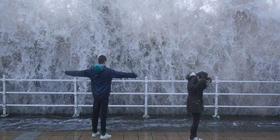 Kinder stehen in Aberystwyth (Grossbritannien) an einer Kaimauer während vor ihnen eine Welle aufschlägt. (Symbolbild)